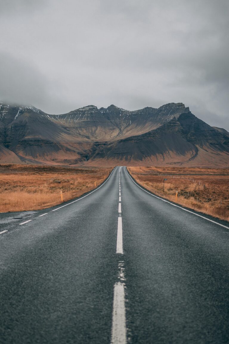 A scenic empty road stretches into snow-capped mountains under cloudy skies, offering a sense of adventure and tranquility.